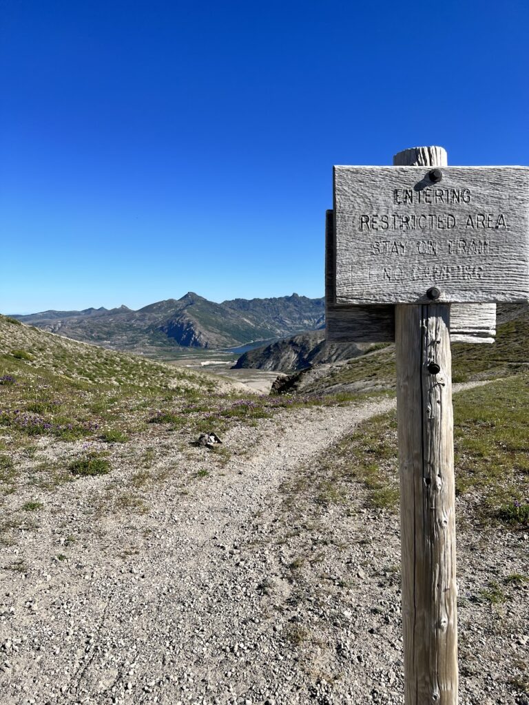 A sign reminding you to stay on path, not to camp, and a view of Spirit Lake.
